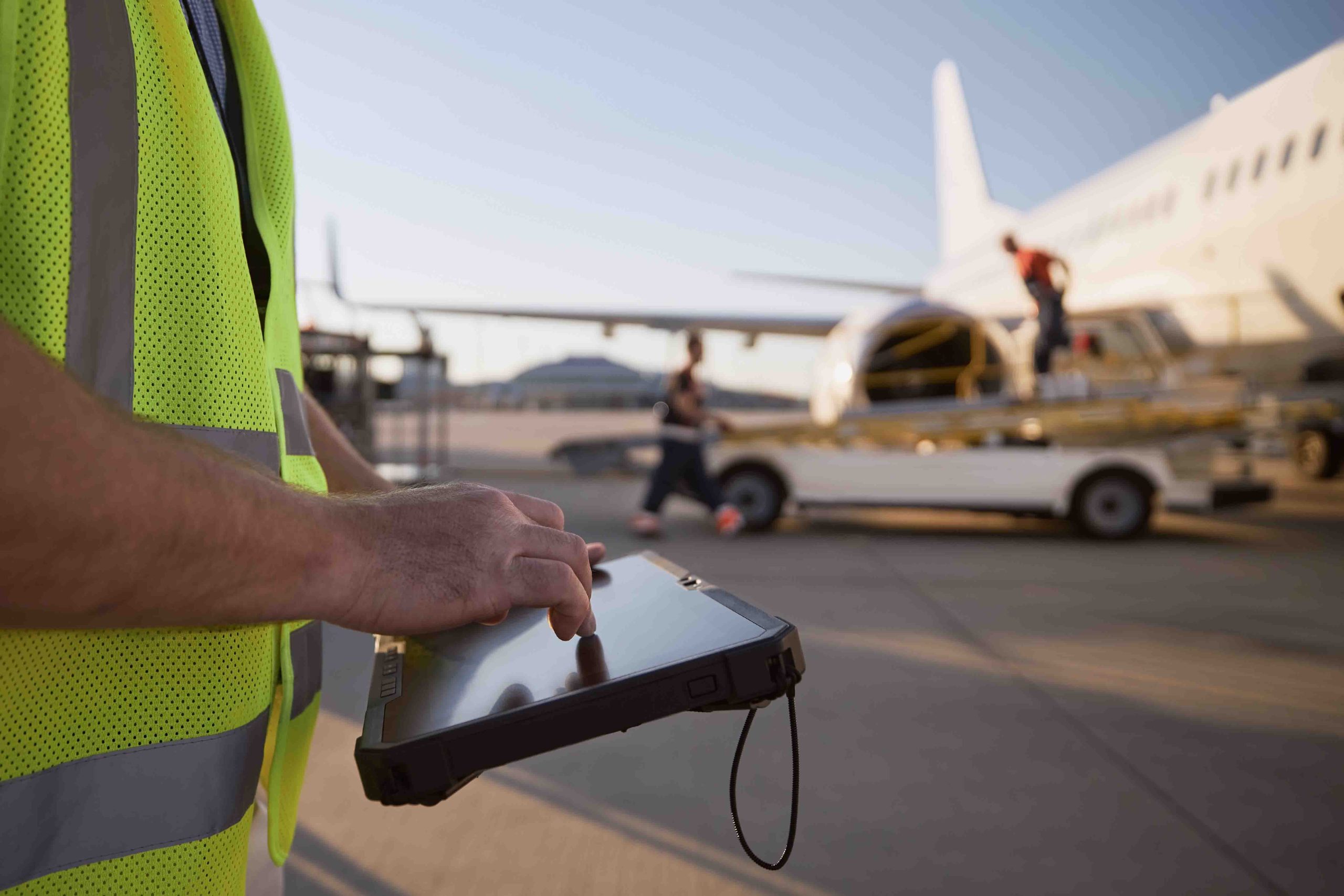 Member of ground crew preparing airplane before flight. Worker using tablet against plane at airport.